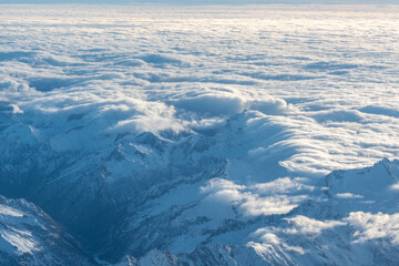 Fototapeta premium Plane view of mountains at sunrise, snow rock and blue cloudy sky aerial view