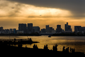 Naklejka premium Silhouetted people relaxing on Odaiba beach during a golden sunset over Tokyo Bay