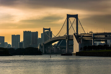 Naklejka premium Scenic view of Odaiba waterfront with suspension bridge and buildings at dusk
