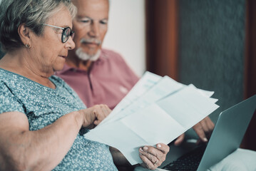 Senior couple reviewing bills and finances at home with laptop, planning retirement and budgeting together © simona