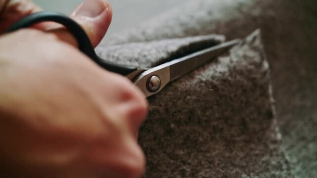 Cutting hands pinching grey felt with fingers guiding scissors on seam at studio forming scrap