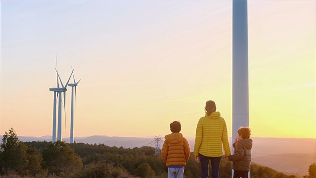 Mother and children stand at sunset watching wind turbines on the horizon, reflecting on clean energy, sustainability and a greener future for the next generation
