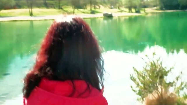 A woman, framed from behind, walks near the shore of Lake Nembia. The woman wears a fuchsia vest and has long dark hair