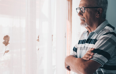 Fototapeta premium Older man in striped polo standing by window looking thoughtful and reflective at home