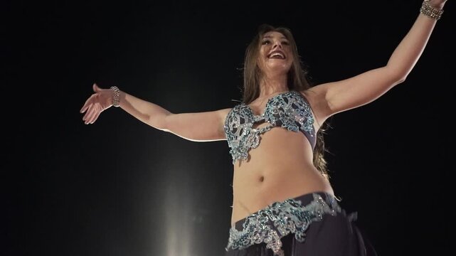 Arab dancer performs belly dance on stage. Black background. Slow motion