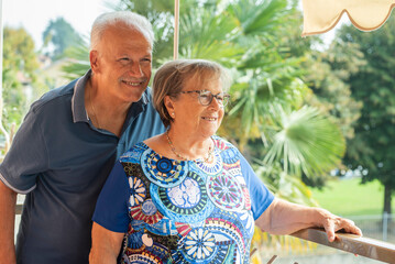 Naklejka premium Smiling senior couple on sunlit balcony enjoying retirement together and relaxed outdoor companionship