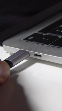 Vertical extreme close-up of a hand connecting a USB Type-C cable into a laptop port. High-quality tech footage for mobile social media, stories, and vertical advertising.