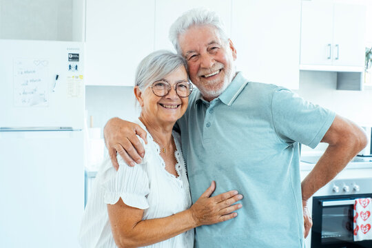 Happy senior couple embracing in a bright modern kitchen, smiling and enjoying home life together