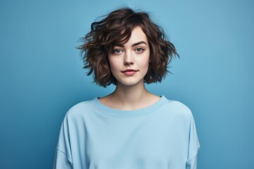 Fototapeta premium Young woman with brown wavy hair and a light blue sweatshirt looking at the camera