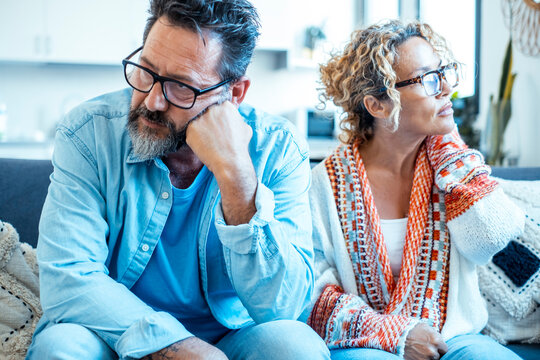 Middle-aged couple sitting apart on couch after an argument, tense and reflective expressions
