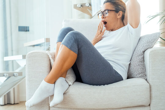 Tired woman yawning on a comfortable sofa in a bright living room relaxing at home