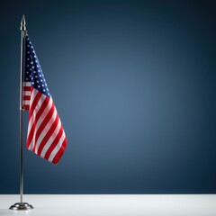 Fototapeta premium American Flag on a Silver Pole Standing Against a Blue Studio Background for Patriotic Government Announcements or Memorial Day Tributes with Copy Space