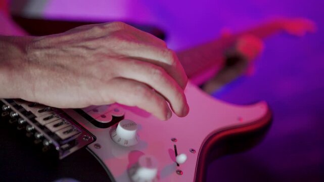Close-up of Musician Playing Electric Guitar on Stage. Guitarist hand strumming strings on a black electric guitar. Professional musician performing under atmospheric red stage lights.