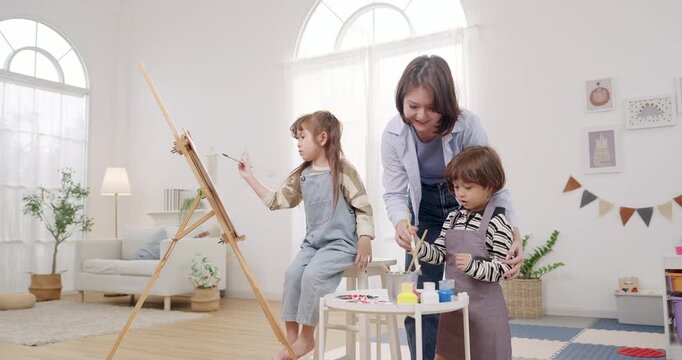 Mom guides preschooler son and daughter painting together on easel canvas, home learning with mom support, sibling teamwork and cooperation, parent child communication and trust, weekend activity
