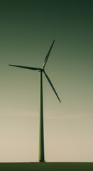 Obraz premium Slender green wind turbine standing in a vast open field against a soft gradient sky for a renewable energy sustainability report and corporate background with copy space