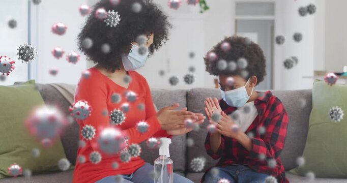Animation of virus cells over african american mother with son disinfecting hands