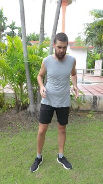 Bearded Man Doing Russian Twist Core Exercise on Green Grass in Tropical Garden