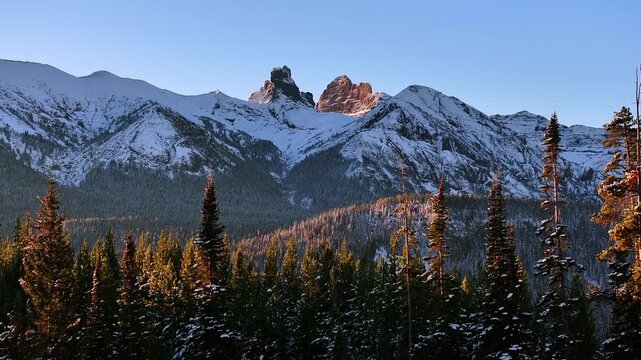 Snow capped mountain peaks above evergreen forest near Cooke City Montana, aerial telephoto establishing overview