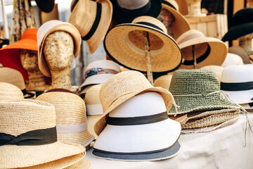 A colorful assortment of straw and fabric hats arranged on mannequin heads and stands at an outdoor market stall, evoking summer style, vacation shopping, vintage charm and casual fashion. © KEA