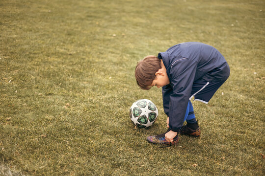 A young boy football player tying the shoelace on his soccer cleat on a backyard football field