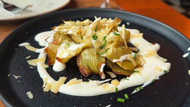 A close-up of fried artichoke flowers flores de alcachofa served on a plate with a creamy truffle sauce. The dish showcases exquisite cuisine, elegant presentation, and beautiful plating, with rich te
