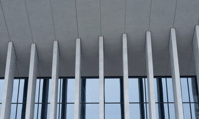 Fototapeta premium Concrete columns support upper slab above glass windows in modern architectural composition. Vertical elements create structured rhythm across facade with strong geometric presence. Concept of public