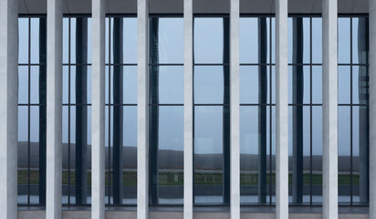Fototapeta premium Glass facade framed by vertical columns reveals interior and distant landscape view. Transparent surface contrasts with solid structural elements in modern building design. Concept of corporate