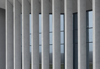 Fototapeta premium Glass windows appear between vertical pillars on modern architectural facade. Transparent panels contrast with solid columns creating structured exterior composition. Concept of office building,