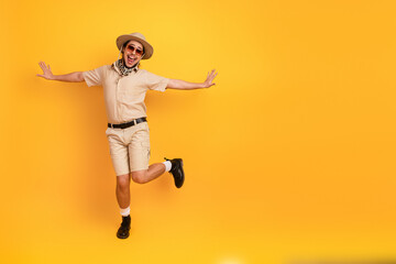Obraz premium Happy explorer in safari outfit jumps for joy against bright yellow background showcasing adventure travel fashion and summer vacation vibe