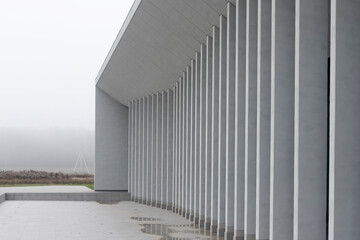 Fototapeta premium Modern building with curved colonnade stands near empty waterfront in minimal landscape. Contemporary structure with repeating vertical columns forms smooth arc along exterior. Architecture concept of