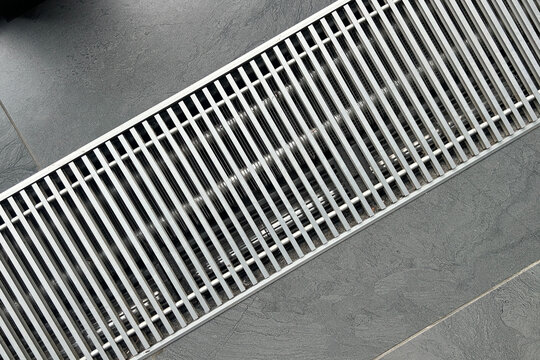 Sleek modern metal linear drain grate with parallel bars on a dark grey textured floor surface