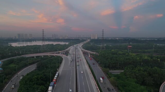 Evening drone shot of highway interchange in Hanoi with warm sky colors, light traffic, and expansive green surroundings under fading daylight