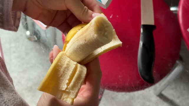 Hands, diet and a person peeling a banana in studio on a gray background closeup for health or nutrition. Fruit, food or healthy eating and a vegan adult with fresh produce for hunger.