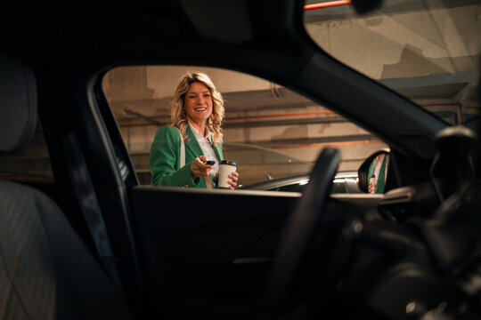 Woman unlocking car in parking garage holding coffee