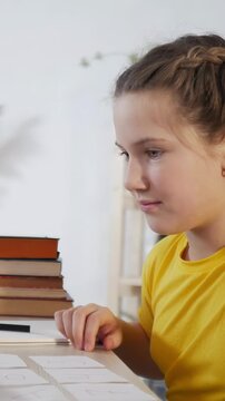 A girl with braided hair is focused on a desk covered with cards. Stacks of books are visible in the background, emphasizing her studious environment.