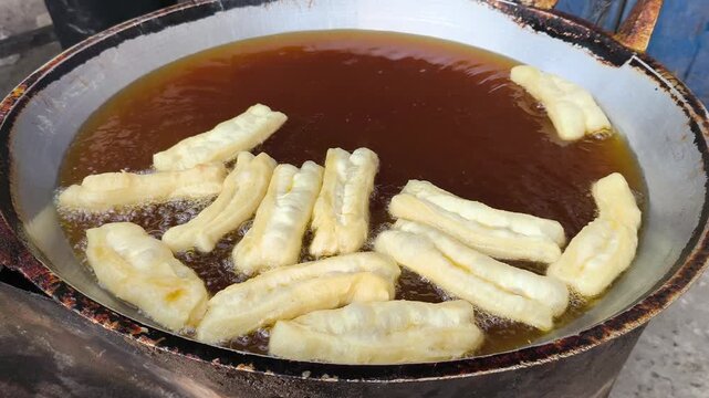 Close-up of cakwe being deep-fried in a large pot of hot oil on a street food stall in Indonesia.