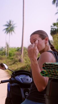 Vertical video. Woman Sitting on Scooter Looking Back and Beckoning with Finger Inviting Viewer to Follow on Tropical Road Surrounded by Palm Trees Slow Motion Travel Adventure Freedom Lifestyle