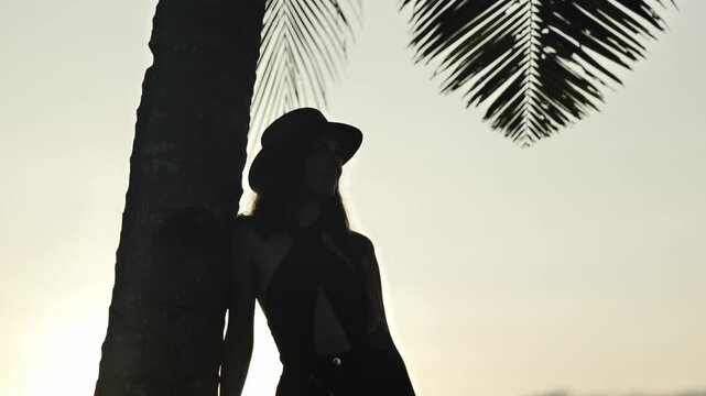 Backlit woman resting by palm trunk at calm sunset in Alegria Cebu Philippines