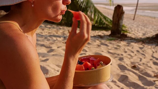 Woman Eating Fresh Pomelo from Bowl While Sitting on Beach Under Palm Trees at Sunset Tropical Lifestyle Healthy Eating Relaxation Close Up