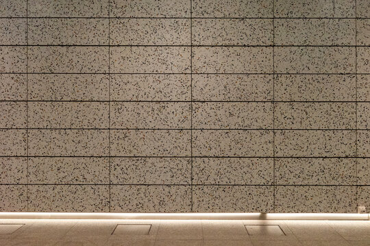A modern architectural interior featuring a wall of rectangular terrazzo tiles with multi-colored stone chips and a glowing LED light strip along the floor base.