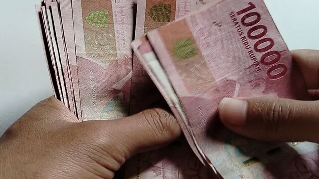 A person counting Indonesian rupiah banknotes of one hundred thousand, financial activity concept, cash handling and money management.