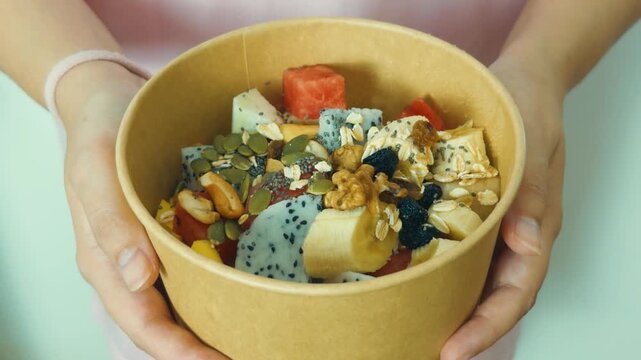Person holding a compostable bowl of vibrant fruit salad with dragon fruit, banana, watermelon, granola, chia, pumpkin seeds, walnuts and cashews for a healthy breakfast snack