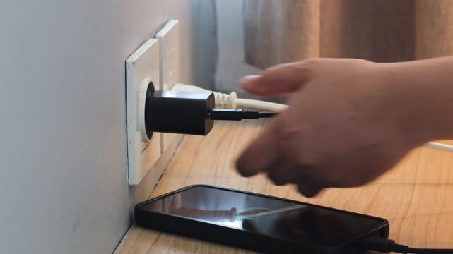 Woman hand view plugging mobile phone charger cable into wall socket. Ready to connect, connect electricity. charging device, electricity usage, home interior daily activity.
