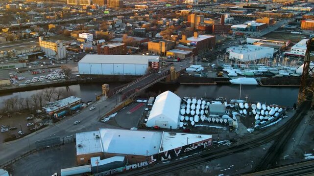 Aerial hyperlapse moving counter-clockwise over an industrial landscape at golden hour, featuring warehouses, highways, roads, and warm sunset light across the urban area.