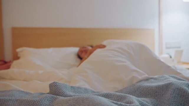 Asian woman hidden under hotel duvet, blue throw in foreground and bedside lamp casting warm glow. Frames show latenight commuter curled fetal, jetlagged guest turning, early dawn sleeper slowly