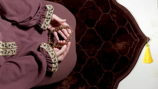 Muslim hands holding prayer beads while sitting on prayer mat during worship. Concept of Islamic prayer, spirituality, devotion, and Ramadan reflection