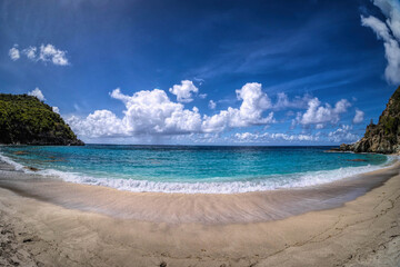 Obraz premium Breathtaking wide-angle view of Shell Beach in St. Barts showcases a pristine curve of light golden sand where gentle waves with white foam roll onto the shore from the vibrant turquoise Caribbean.