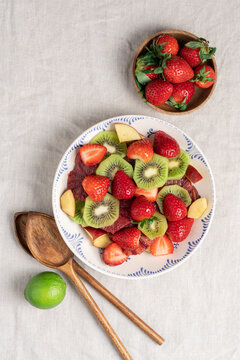 Fresh summer fruit salad with strawberries and kiwi in ceramic bowl on table with linen tablecloth, healthy seasonal dessert concept