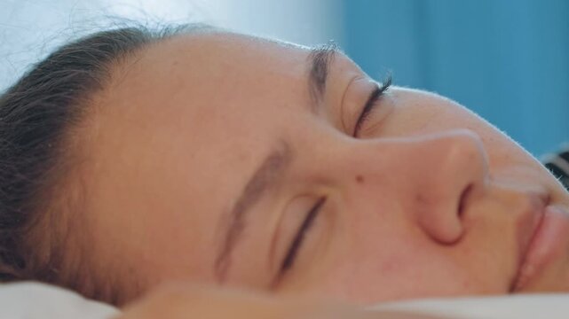 Closeup business traveler waking on pillow in hotel room, blue curtain background, subtle eyelid movement, jetlagged expression, morning light, quiet fatigue before day of meetings