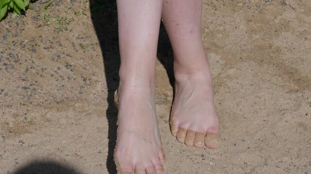 Close up of young womans legs on warm sand under bright sunlight. She is moving her toes while enjoying a beach vacation. Summer holiday and relaxation concept.